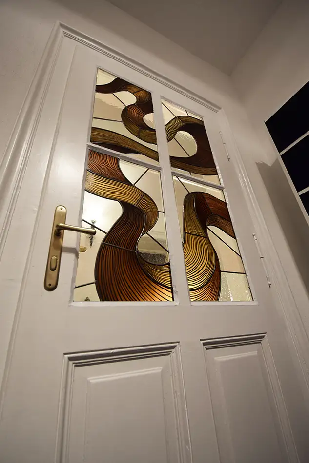Stained glass window with a painted depiction of a serpentine ribbon in shades of brown and beige