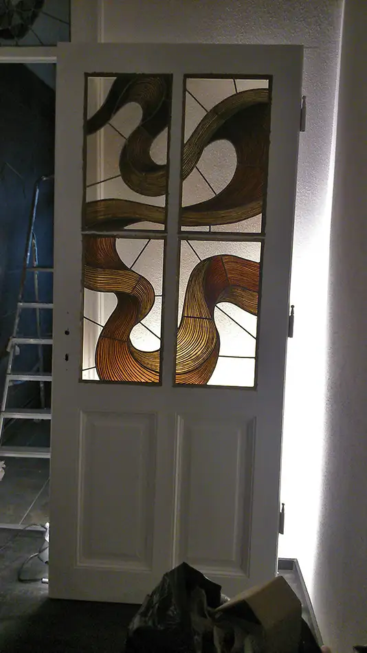 Atained glass window with a painted depiction of a serpentine ribbon in shades of brown and beige