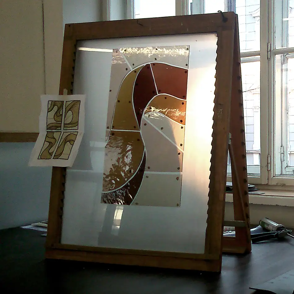 Production process of a stained glass window with a painted depiction of a serpentine ribbon in shades of brown and beige