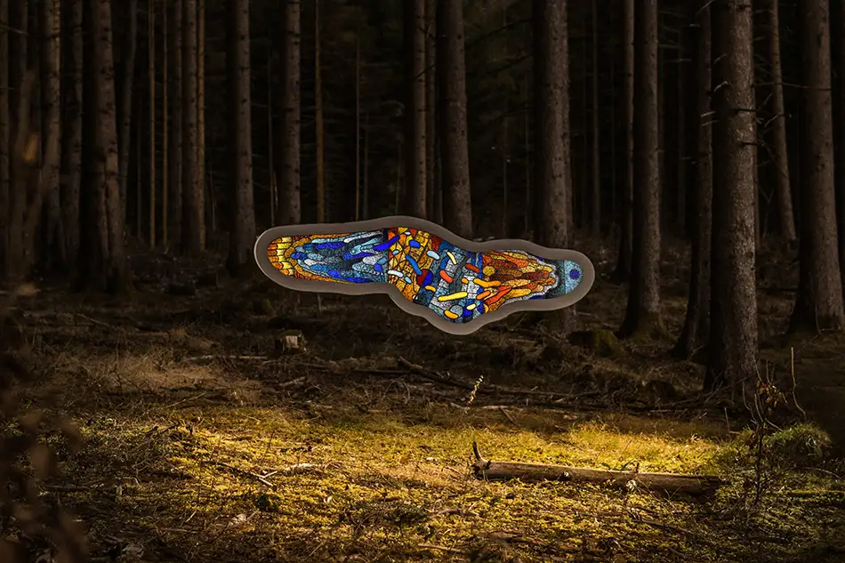 Frontalansicht einer frei hängenden und beleuchteten Bleiverglasung mit dem Namen Amoeba die in einem Wald hängt