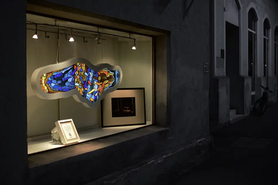 Ausstellungsansicht einer frei hängenden und beleuchteten und detailliert bemalten Bleiverglasung mit dem Namen Amoeba