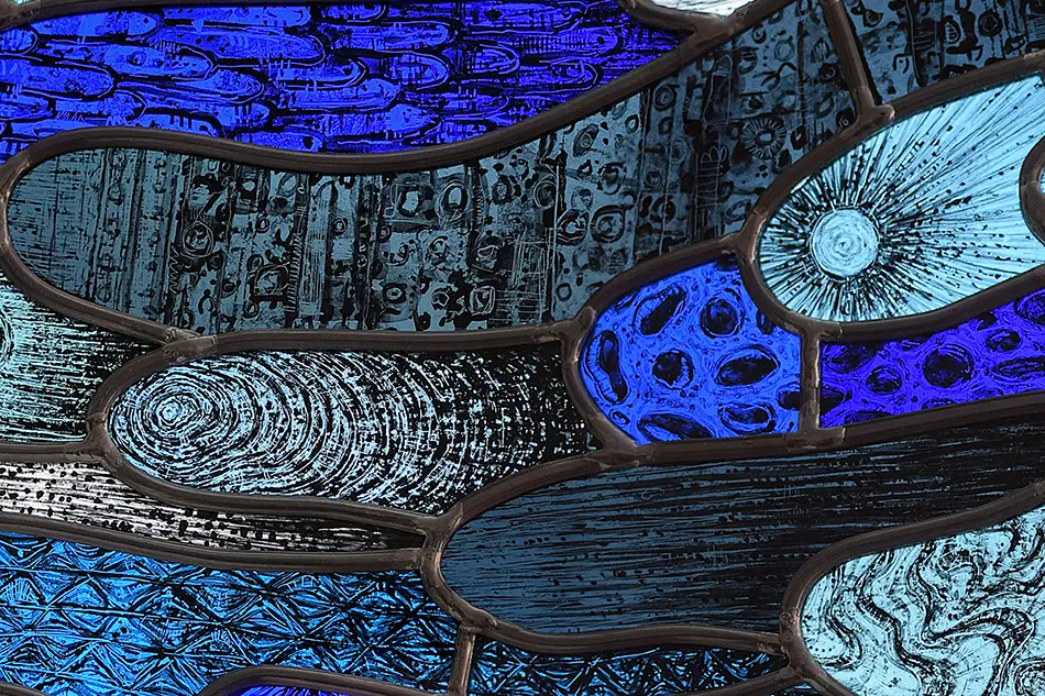 Detail of a free-hanging and illuminated stained glass window with detailed painting which is named Amoeba and hangs in a forest