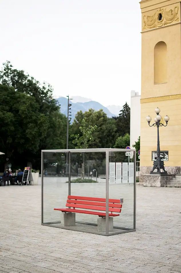 Kunstinstallation im öffentlichen Raum die eine eingeglaste Parkbank zeigt mit dem Titel Nehmen Sie Platz!