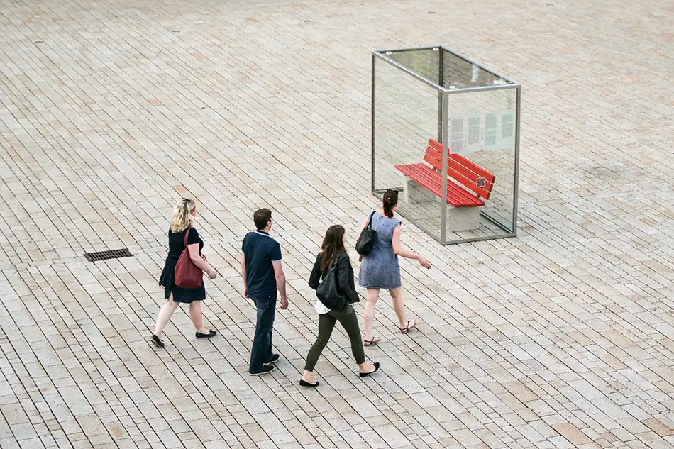 Personen vor Kunstinstallation im öffentlichen Raum die eine eingeglaste Parkbank zeigt mit dem Titel Nehmen Sie Platz!
