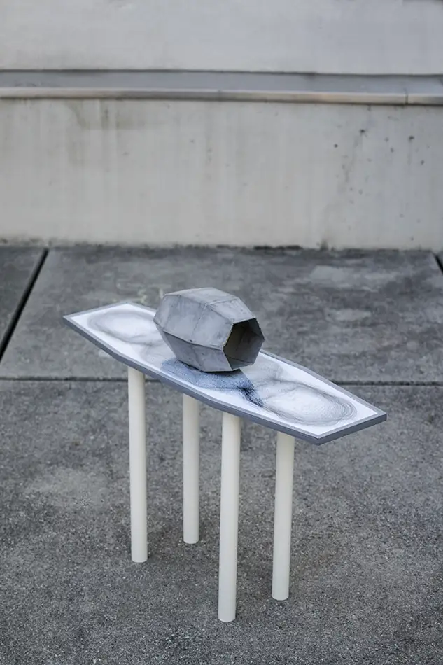 artwork made of concrete, mirror and digital print which is reminiscent of a table on which a geometric concrete element stands in the centre of which a mirror is fixed.