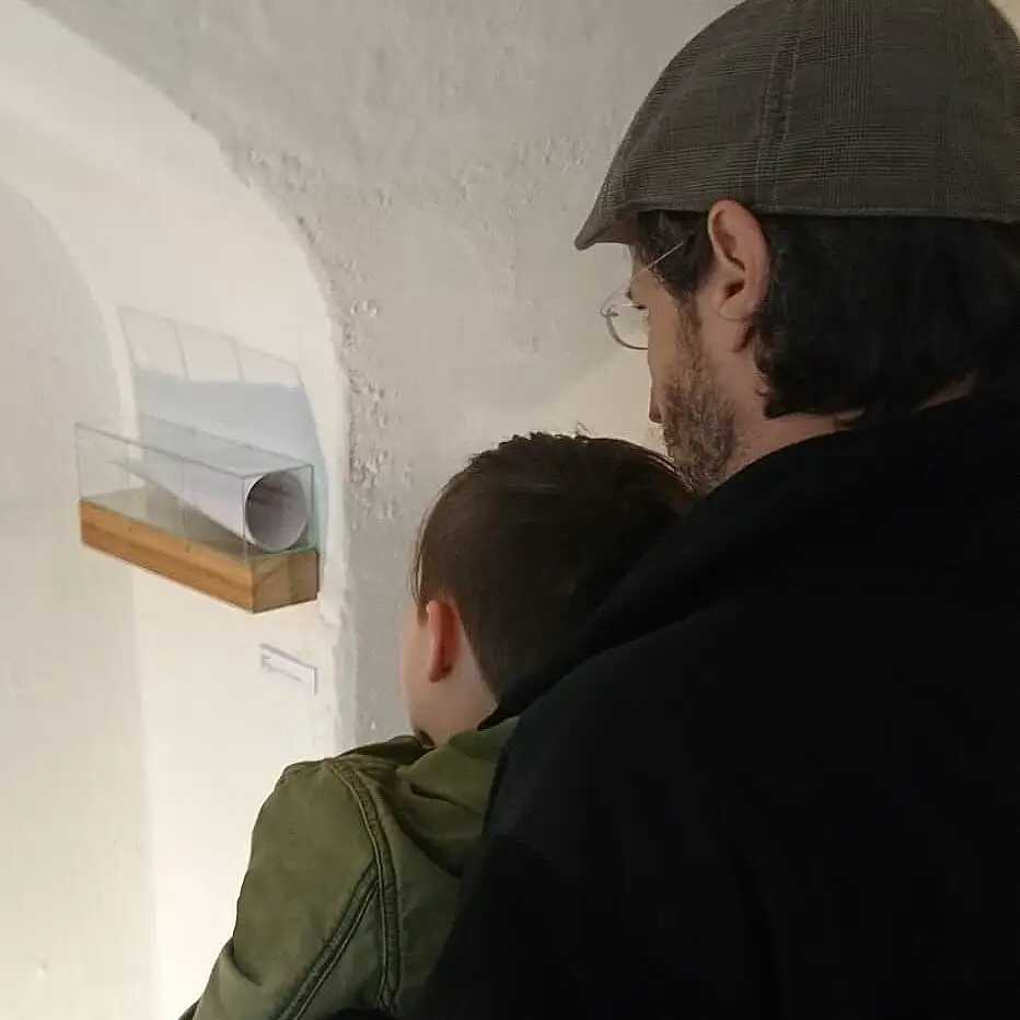 anamorphe installation aus Glas und einer Bleistiftzeichnung bei der ein Auge in einem Kegel sichtbar ist - Ausstellungsansicht mit Kind und Vater