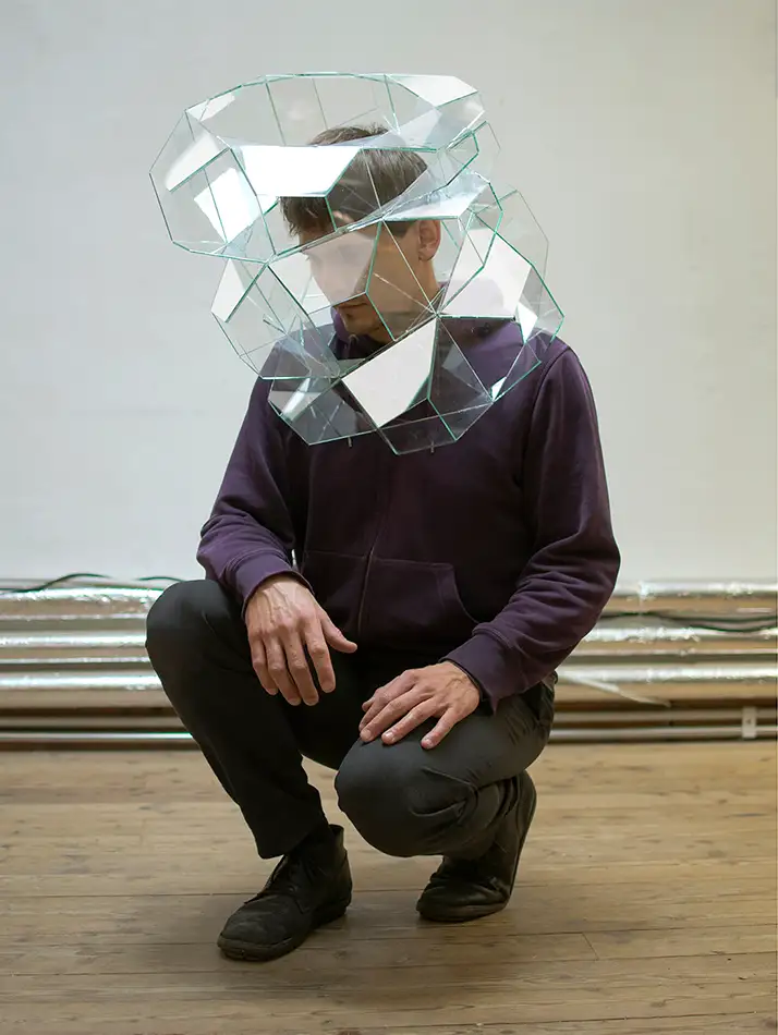 A geometric glass sculpture made of colourless glass that is placed over the head of a person