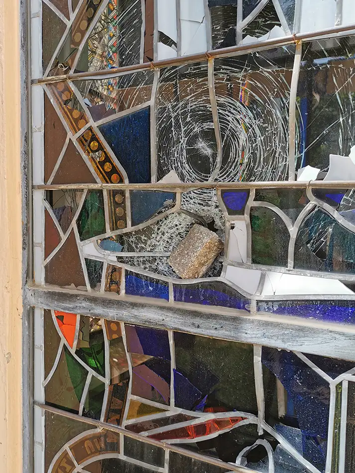 Neuanfertigung von Bleiverglasungen für die Dominikanerkirche Eppan - Pflasterstein steckt in dem Fenster vor der Neu-Anfertigung